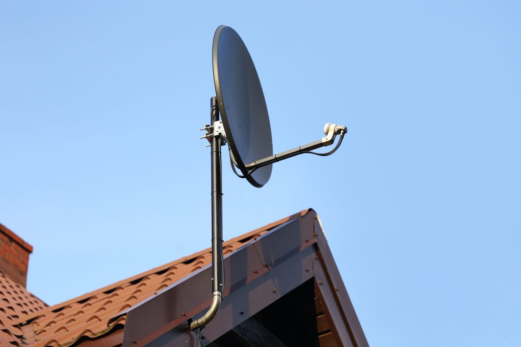 A satellite dish on a pole above a red tiled roof
